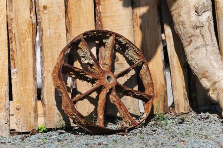 The old rusty iron wheel leaning against a wooden fenceの写真素材