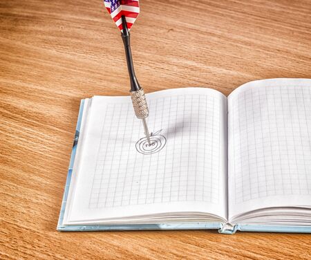 Needle of a dart on a notebook, an apple is drawn, a target