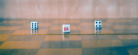 Dice on a wooden background on a chessboard, with dark and light squares, very popular all over the world board games accessoriesの写真素材