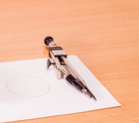 A compass on a sheet of paper A wooden background is a very useful tool by which to draw a circle