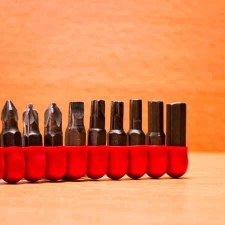 Red case with nozzles of various shapes for screwdrivers on a wooden background
