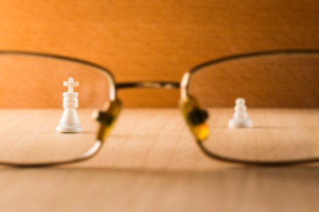 White king and pawn view through glasses of eye glasses on a wooden backgroundの写真素材