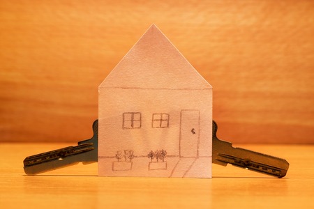 Paper house and metal keys to it on a wooden backgroundの写真素材