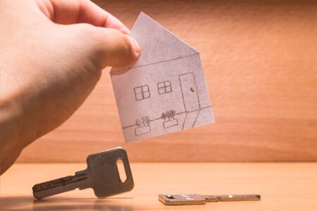 paper house in hand on a wooden background at the bottom metal keysの写真素材