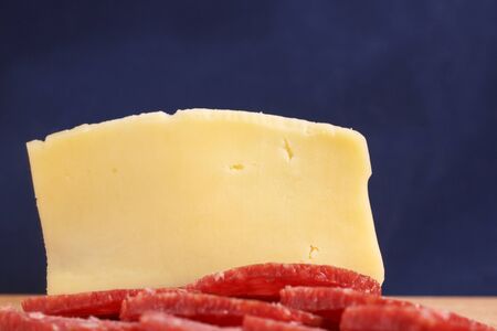 appetizing slice of cheese and sliced smoked sausage on a blue background