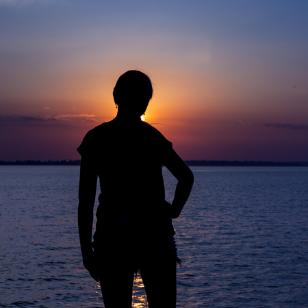silhouette of a girl at sunset against a beautiful estuaryの写真素材