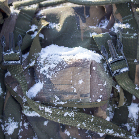 military backpack covered with fluffy white snow close-up on a bright winter dayの写真素材