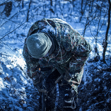 guy in camouflage with a shovel in the winter winter forest he bent down and looks for somethingの写真素材