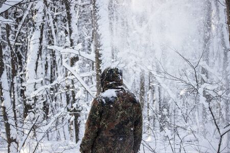 back of a traveler in camouflage against a white winter forest the snow is falling brightly and...
