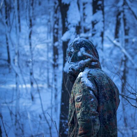 mysterious man in military uniform alone in the winter forest at night exciting and terrible atmosphere maybe under the hood hiding maniacの写真素材