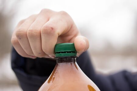 guy opens a plastic bottle of beer with a green lid close upの写真素材