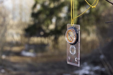 Compass with a transparent ruler hangs on a yellow cord on the blurred background