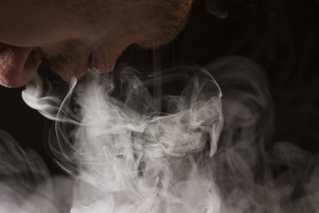 addict exhales cigarette smoke on a dark background concept of combating smoking and bad habitsの写真素材