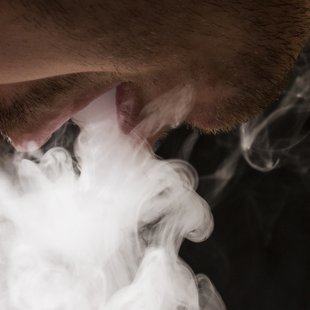 the smoker opened his mouth and lets out a cloud of cigarette smoke on a dark background the concept...