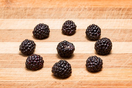 bright blackberries on a striped wooden board are lined around and one in the middle stands out among the restの写真素材