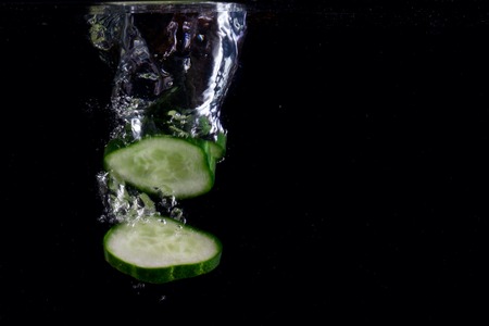 pieces of cucumber go to the bottom on a dark background concept of food and vegetablesの写真素材
