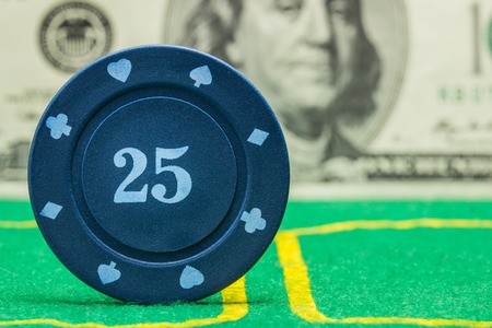 bright blue poker chip on a green canvas closeup on a blurry background of dollar bill concept of casino and gamblingの写真素材