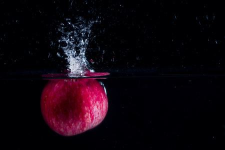 red apple fallen in the water on a dark background formed a beautiful splash on the surface of the concept of eatingの写真素材