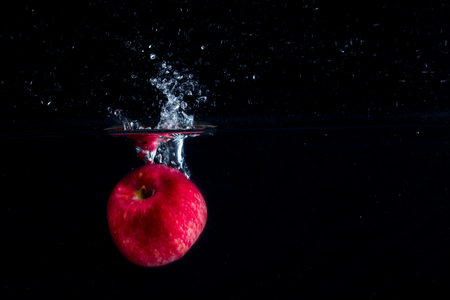 red apple sinks in the water on a dark background forming a beautiful splash on the surface of the concept of eatingの写真素材