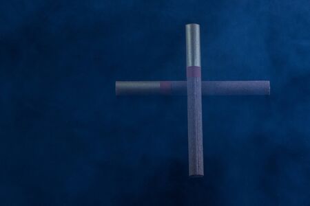 cross laid out of two cigarettes lies in blue smoke mysterious atmosphere concept of addictionの写真素材
