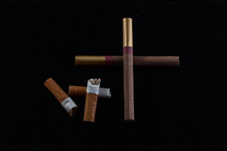 cross laid out of cigarettes and cigarette butts lie next to on a dark background the concept of smoking and bad habitsの写真素材
