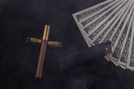 cross made of cigarettes and cigarette butts a lighter and one hundred dollar bills lie in the smoke...