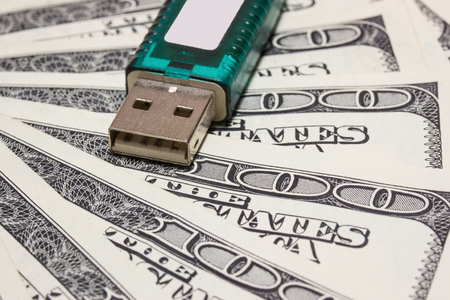 a flash drive with a green case lies on a fan of one hundred dollar bills close-up the concept of...