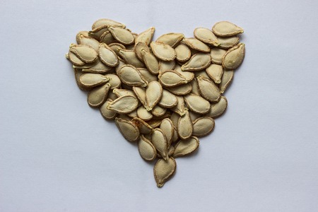 pumpkin seeds laid out in the shape of a heart on a sheet of paper close up concept nature and...