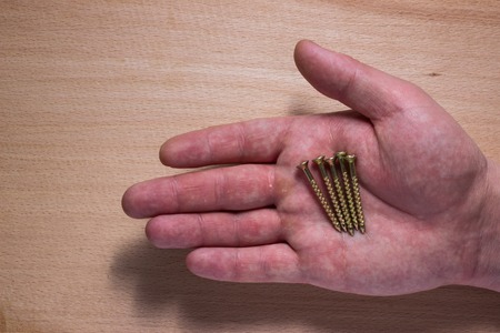 five golden screws lie in the palm of a worker close up on a wooden background industry conceptの写真素材