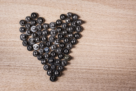 dark silver heart lined with small metal screws on wooden background close up concept of industry...