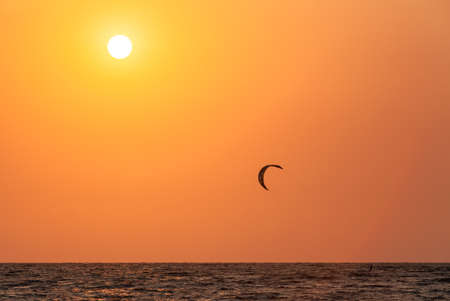 an athlete kitesurfing against the background of an orange sunset by the oceanの写真素材