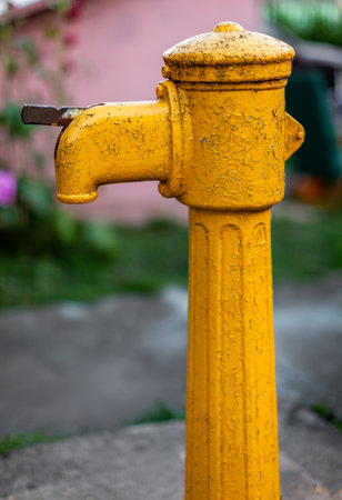 old metal water column painted yellow standing in the garden. High quality photo