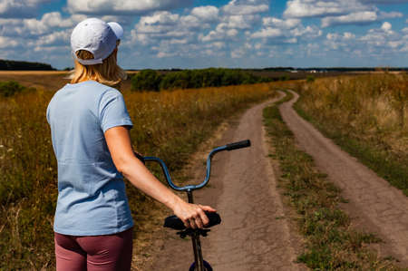 woman standing with a bicycle on a country road looking into the distance. High quality photoの写真素材
