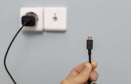 micro usb wire in hand against the background of the power supply. High quality photoの写真素材
