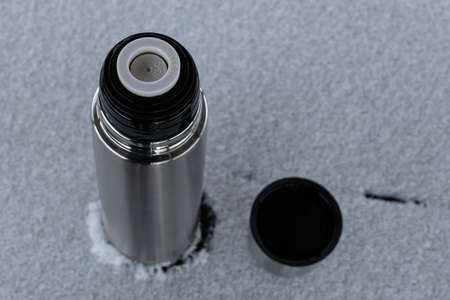 a metal flask with an open lid stands on a snowy table. high quality photo