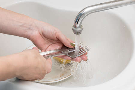 female hand in the sink washes a dirty fork in water. high quality photoの写真素材