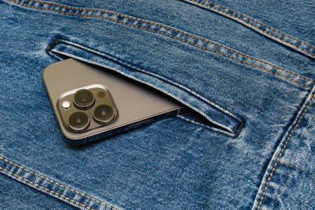 a gray smartphone sticks out of the side pocket of a denim jacket