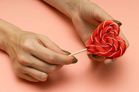 a woman's hand holds a red heart-shaped lollipop. high quality photo