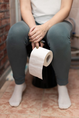 woman sitting on the toilet holding a roll of paper. high quality photoの写真素材