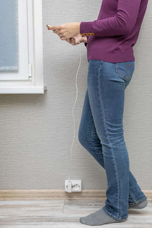 a woman stands near a socket with a phone in her hand that is charging. high quality photo