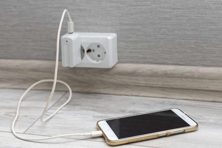 smartphone lies on the floor connected to the charger. high quality photo