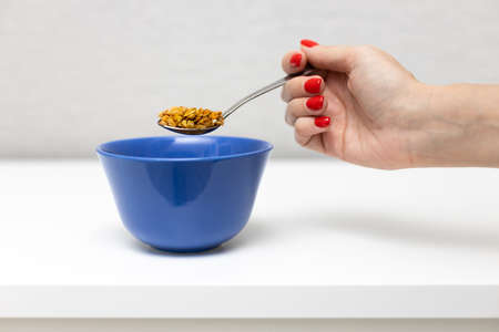 female hand holds a spoon with cereal over a cupの写真素材