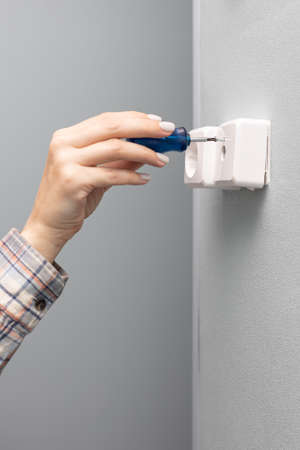 a woman unscrews with a screwdriver repairing a television wall socket. high quality photo
