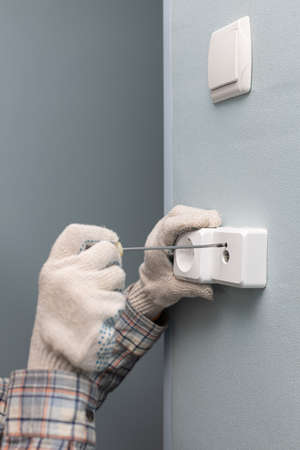 a man unscrews with a screwdriver repairing a television wall socket