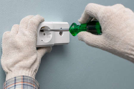 a man screwing a wall electrical socket with a screwdriver