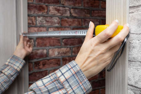 a woman measures a doorway in a house with a tape measureの写真素材