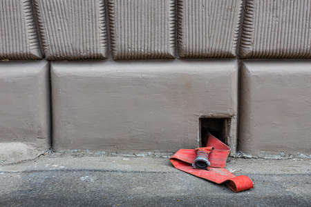 a fire hose lies on the asphalt peeking out of a hole in the wall. high quality photoの写真素材