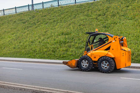 Moscow, Russia - May 21, 2022: a miniature tractor with a bucket rides down the street. high quality...