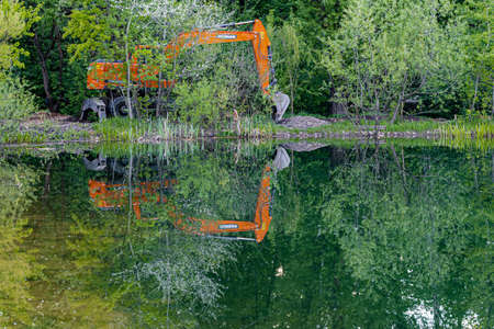 Moscow, Russia - May 21, 2022: excavator digs the ground on the shore of a reservoir. high quality photoのeditorial素材