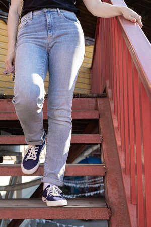 female legs in jeans and sneakers go down the stairs. high quality photo